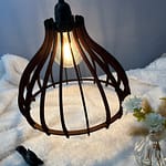 Suspension en bois Boréa couleur acajou, avec on ampoule allumé. Disposée au-dessus d'une nappe en velour et à côté d'un écureuil en 3D et d'un vase en verre