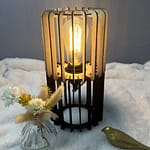 Lampe en bois vanille-chocolat avec son ampoule allumée. Disposée sur une nappe en velour à côté d'un oiseau 3D et d'un vase en verre.