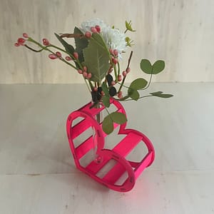 Décoration coeur "Adoration" en bois en rose. C'est un coeur qui accueil en son centre un petit vase pour y mettre des fleurs. Le coeur est un peu décalé et en plan large.