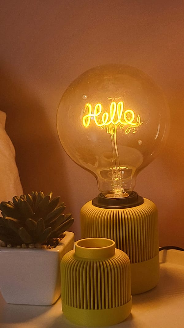 Lampe Solelight en 3D avec ampoule hello jaune sur une table basse de chambre accompagné d'un petit vase solea. Idéal comme lumière d'appoint.