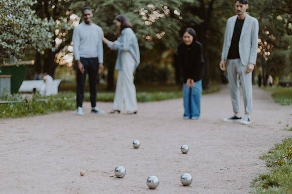 4 personnes en train de jouer à la pétanque sur un chemin. Un compteur de points pétanque en bois serait utile pour suivre la partie facilement. A retrouver sur notre site crea-th.fr