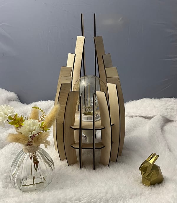 Lampe en bois dubaï, couleur brute avec sa propre ampoule éteinte. Posée sur une nappe en velour à côté d'un lapin 3D et d'un vase avec des fleurs en bois