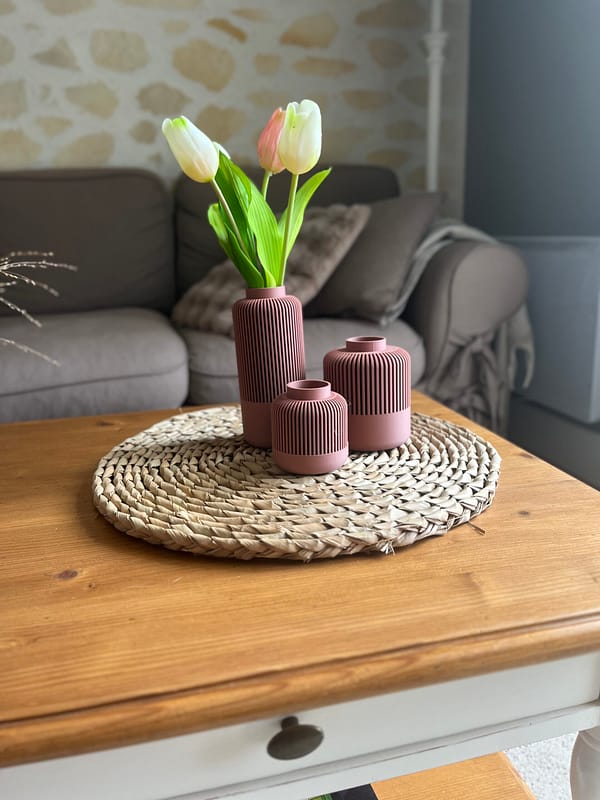 3 vases Solea emboîtables mauve sur un tapis en bois. 3 vases de tailles différentes, le plus grand contient des tulipes blanches. Prise de vue plus lointaine