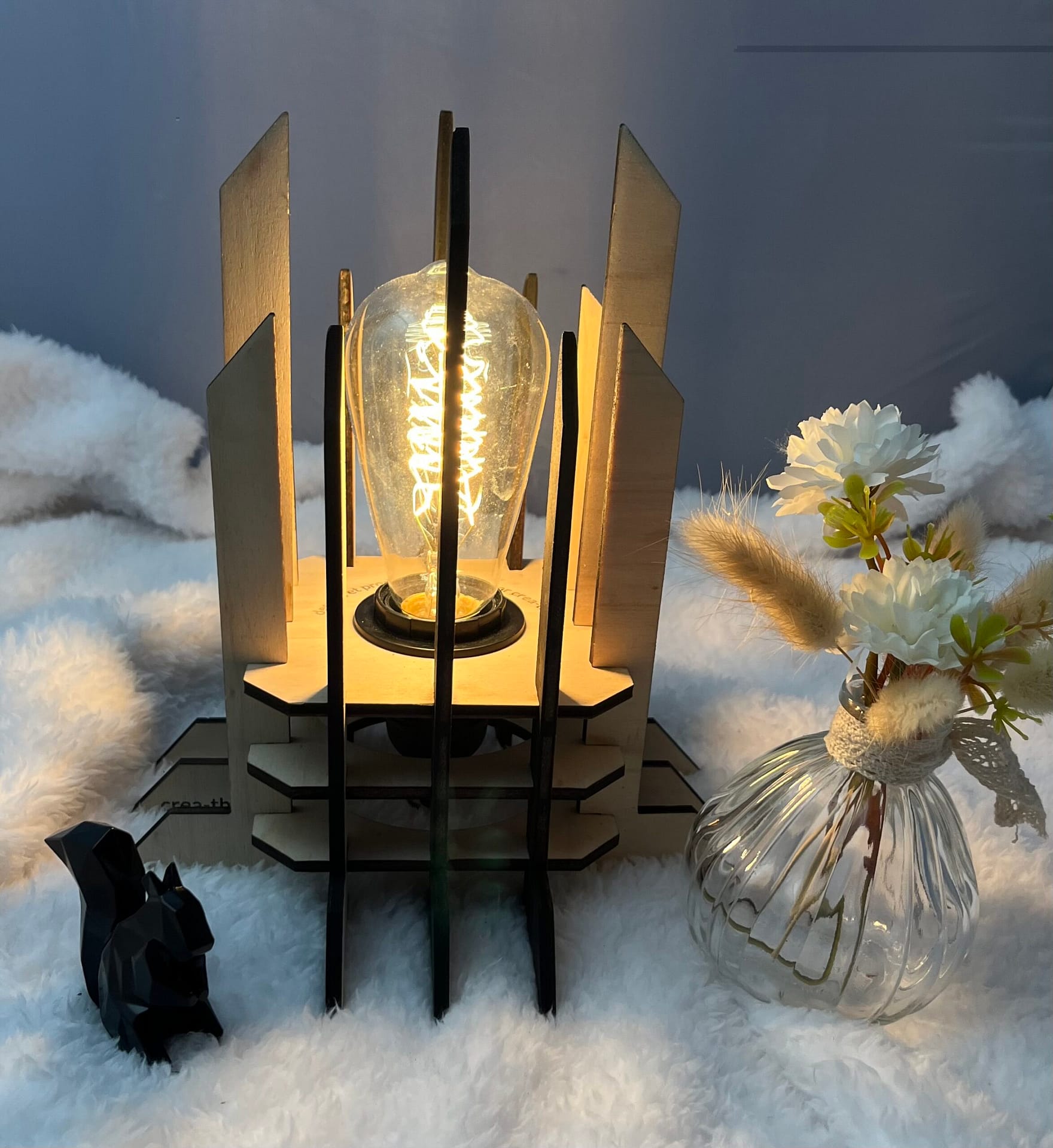 Lampe Luxor en bois moderne. Elle est réversible avec ses deux couleurs noir et blanc. La lampe est posée sur une nappe en velour avev un écureuil en 3D et un pot de fleur à côté