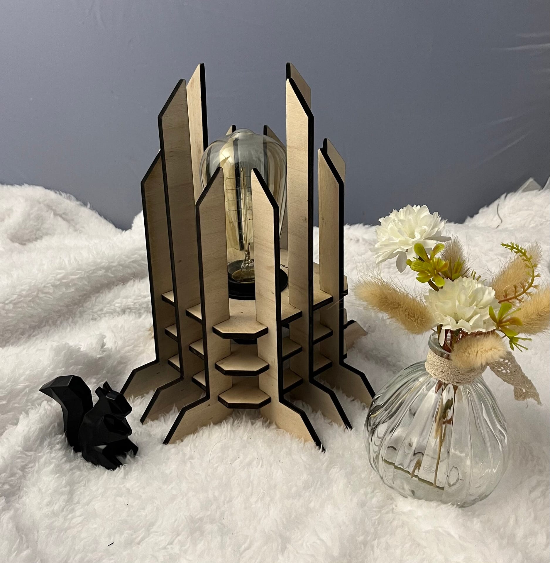 Lampe Luxor en bois moderne. Elle est réversible avec ses deux couleurs noir et blanc. La lampe est posée sur une nappe en velour avev un écureuil en 3D et un pot de fleur à côté