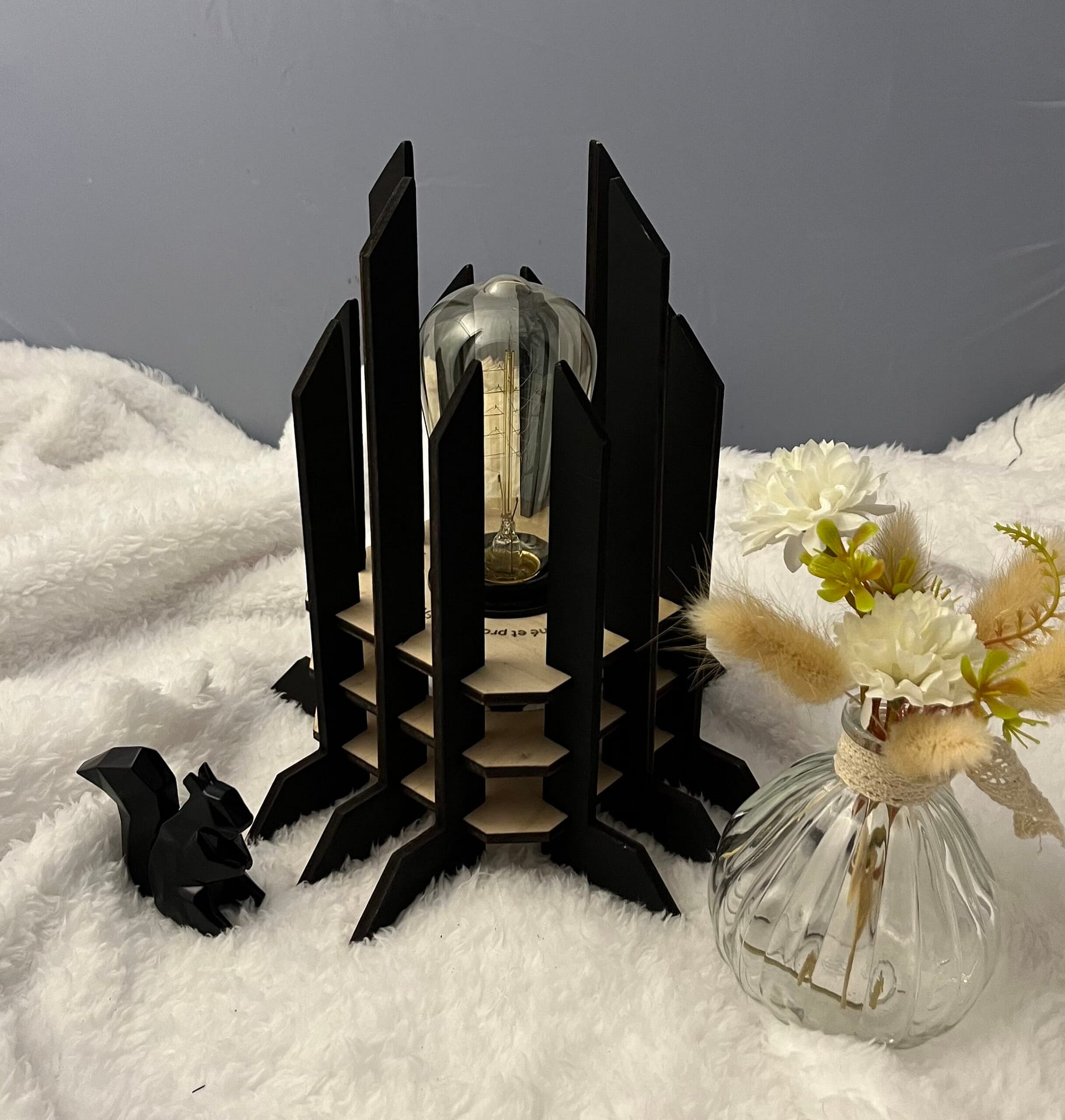 Lampe Luxor en bois moderne. Elle est réversible avec ses deux couleurs noir et blanc. La lampe est posée sur une nappe en velour avev un écureuil en 3D et un pot de fleur à côté