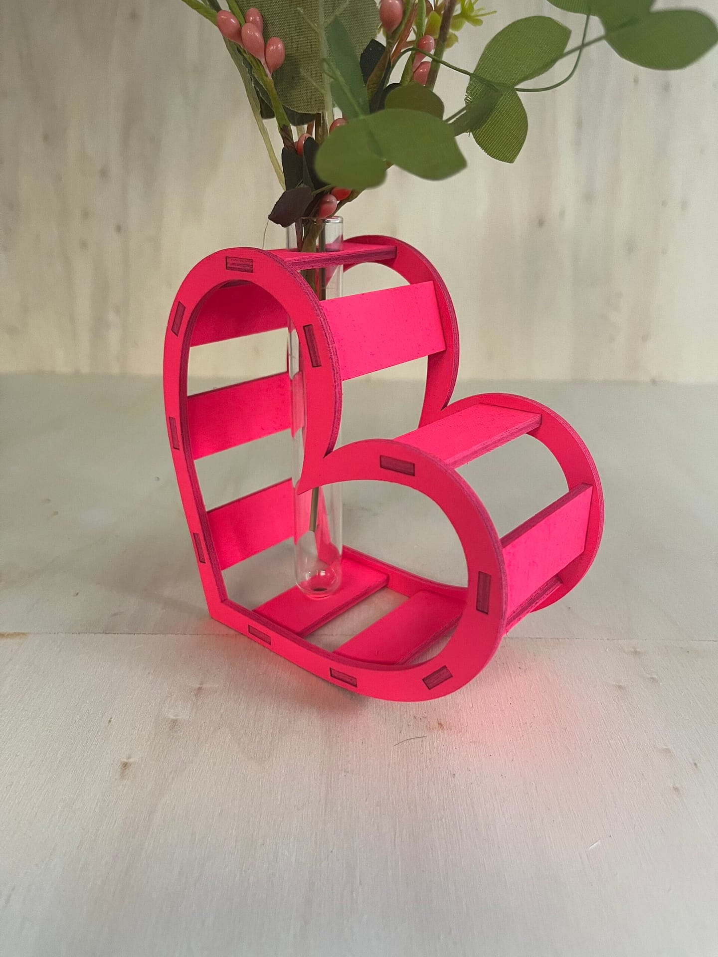 Décoration coeur "Adoration" en bois en rose. C'est un coeur qui accueil en son centre un petit vase pour y mettre des fleurs. Le coeur est un peu décalé et en plan serré.