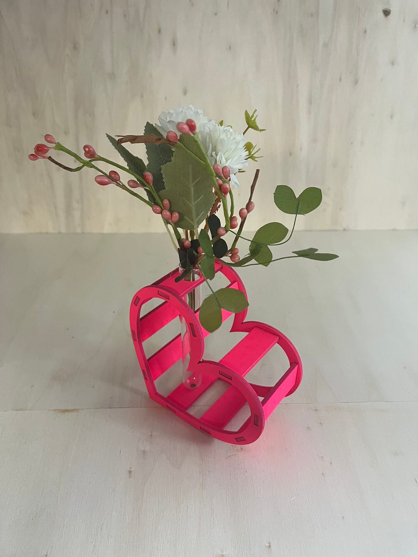 Décoration coeur "Adoration" en bois en rose. C'est un coeur qui accueil en son centre un petit vase pour y mettre des fleurs. Le coeur est un peu décalé et en plan large.